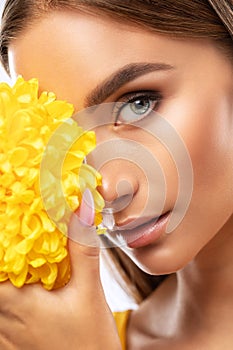 Portrait of an attractive girl with healthy clean skin and beautiful makeup, she is holding a yellow chrysanthemum. Aesthetic