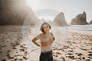 Portrait of attractive girl with light brown hair posing on rocky Ursa beach on sunset. Smiling looking to the camera