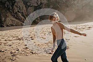 Portrait of attractive girl with light brown hair running on rocky Ursa beach on sunset. Smiling looking to the camera