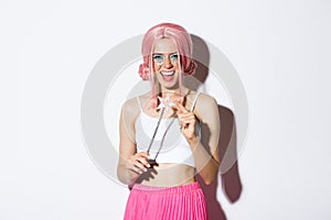 Portrait of attractive girl with pink wig and bright makeup, dressed up as a fairy for halloween party, holding magic