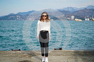 Portrait of attractive girl wallking near to sea in summer. Stylish pretty woman with long hair wearing sunglasses