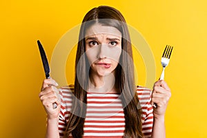 Portrait of attractive girlish hungry girl holding cutlery biting lip waiting meal  over bright yellow color