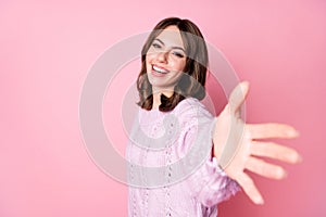 Portrait of attractive glad cheerful wavy-haired girl giving you hand come with me  over pink pastel color