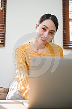 Attractive Asian woman using laptop computer in her living room, working from home