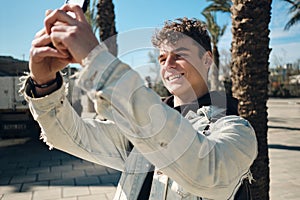 Portrait of attractive guy joyfully taking photo on smartphone outdoor