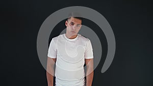 Portrait of attractive and handsome young man stands in white shirt and looks on camera. Isolated on black background