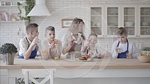 Portrait attractive happy woman and her four teen sons eating pies and drinking orange juice in the kitcken standing at