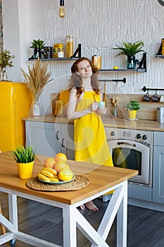 Portrait of an attractive healthy red-haired girl in a yellow sundress with fruit in her hands in the kitchen