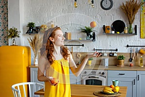 Portrait of an attractive healthy red-haired girl in a yellow sundress with fruit in her hands in the kitchen. Throws up an orange