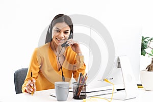 Portrait of attractive hotline assistant woman wearing microphone headset speaking with customer while sitting at her workplace in