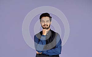 Portrait of attractive Indian man propping chin with his hand on lilac background