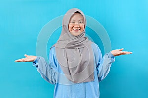 Portrait of attractive Indonesian glad cheerful girl holding on two palms copy empty blank space offer isolated over blue color