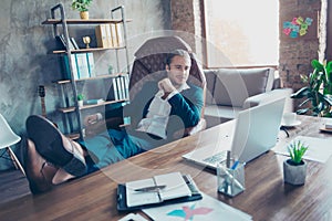 Portrait of attractive lawyer sitting at his desk in work place, putting legs with shoes on table, enjoying break time, watching