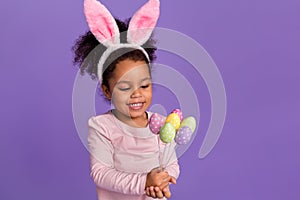 Portrait of attractive little small trendy pre-teen girl holding handicraft eggs isolated over bright purple violet