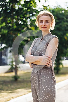 Portrait of attractive looking 40 years old woman standing half turn outdoors among green trees with pleasant smile