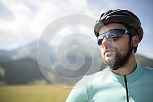 Portrait of attractive male cyclist, riding bike across beautiful nature, wearing helmet, sunglasses. Concept of healthy