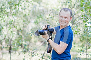 Portrait of attractive male photographer wearing blue t-shirt outdoors on Summer day. Young man with a DSLR camera in hands