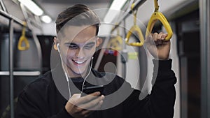 Portrait of attractive man in headphones holds the handrail, listening to music and browsing on mobile phone in public