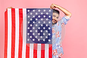 Portrait of attractive man holding USA flag in hands, looking at camera with toothy smile, proud of