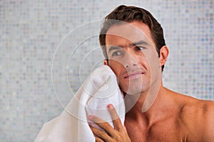 Portrait of attractive man wiping his face with towel in bathroom