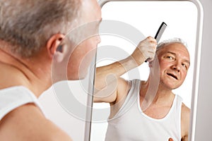 Portrait of attractive middle aged, 45s man looking to mirror while combing his grey hair against white background.