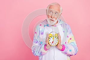 Portrait of attractive minded grey-haired man holding clock thinking copy space isolated over pink color background