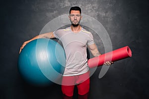 Portrait of attractive muscular caucasian man holding a medical ball and a training mat,