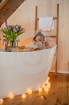 Portrait of attractive naked woman relaxing and spending weekend at home. Taking bath with glass of wine on food tray