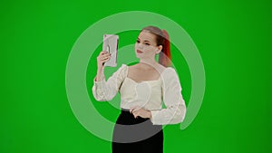 Portrait of attractive office girl on chroma key green screen. Woman in skirt and blouse talking by video call on tablet