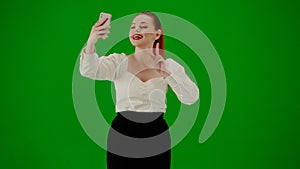 Portrait of attractive office girl on chroma key green screen. Woman in skirt walking and taking selfie on smartphone