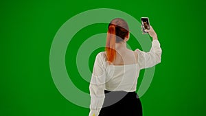 Portrait of attractive office girl on chroma key green screen. Woman in skirt walking and taking selfie on smartphone