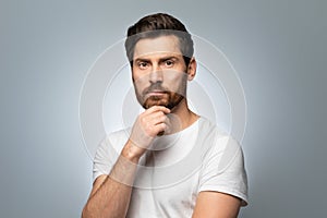 Portrait of attractive perfect well-groomed middle aged man touching chin and looking at camera, grey background