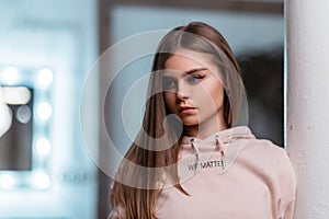 Portrait of an attractive pretty young woman with long brown hair with natural make-up in a fashionable pink sweatshirt indoors.