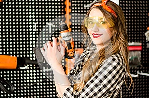 Portrait of the attractive salesgirl with long blonde hair and yellow glasses in home improvement store with a drill