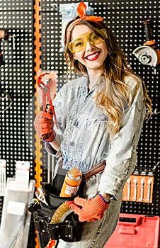 Portrait of the attractive salesgirl with long blonde hair and yellow glasses in home improvement store with pliers