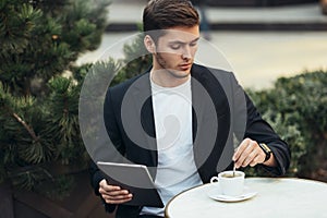 Portrait of attractive and serious  Caucasian man in casual suit typing messages in social networks with morning coffee break.