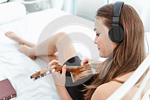 Portrait of Attractive Sexy Woman is Relaxing on Bedroom While Playing Ukulele Instrument and Listen Music on Headphones on