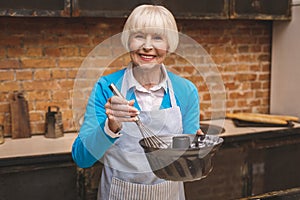 Portrait of attractive smiling happy senior aged woman is cooking on kitchen. Grandmother making tasty baking