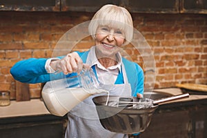 Portrait of attractive smiling happy senior aged woman is cooking on kitchen. Grandmother making tasty baking