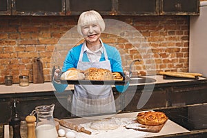 Portrait of attractive smiling happy senior aged woman is cooking on kitchen. Grandmother making tasty baking
