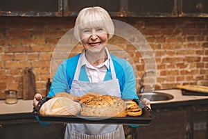 Portrait of attractive smiling happy senior aged woman is cooking on kitchen. Grandmother making tasty baking