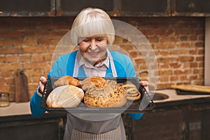 Portrait of attractive smiling happy senior aged woman is cooking on kitchen. Grandmother making tasty baking