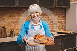 Portrait of attractive smiling happy senior aged woman is cooking on kitchen. Grandmother making tasty baking