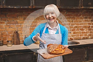 Portrait of attractive smiling happy senior aged woman is cooking on kitchen. Grandmother making tasty baking