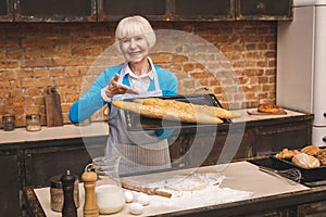 Portrait of attractive smiling happy senior aged woman is cooking on kitchen. Grandmother making tasty baking