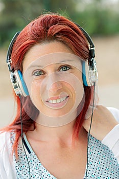 Portrait of an attractive smiling redhead woman listening to music on her phone with greenery in the background