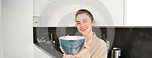 Portrait of attractive smiling woman giving you cup, offering morning coffee and looking happy, standing in the kitchen