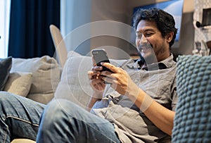 Portrait of an attractive smiling young bearded man wearing casual clothes sitting on a couch at the living room