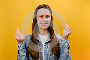 Portrait of attractive smiling young woman 25s looking at camera with money or italian gesture with hands, wearing denim jacket,