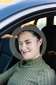 Portrait of an attractive and smiling young woman in her 30\'s inside her car looking at the camera.